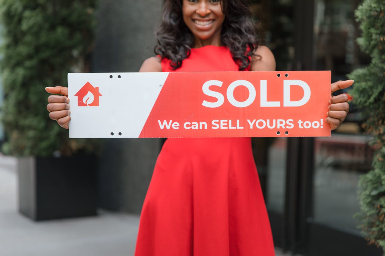 Smiling woman holding a Sold sign, symbolizing successful real estate sales.